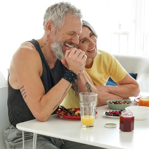 Happy mature husband and older wife having fun eating breakfast at home.