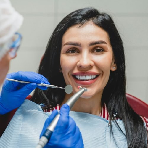 Orthodontist applying veneers, whitening her teeth, filling tooth, curing caries decay. Stomatology